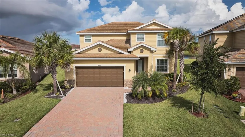 View of front of home featuring a tiled roof, decorative driveway, stone siding, a front lawn, and stucco siding