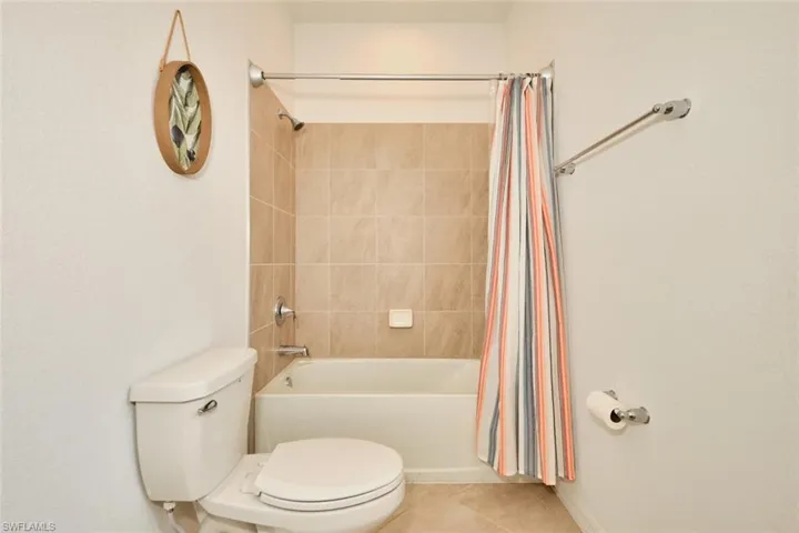 First floor Full bath featuring a closet, vanity, light tile patterned flooring, and a tub/shower with shower curtain