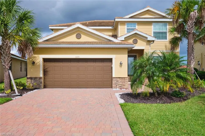 View of front of property with stone siding, decorative driveway, stucco siding, a garage, and a front yard