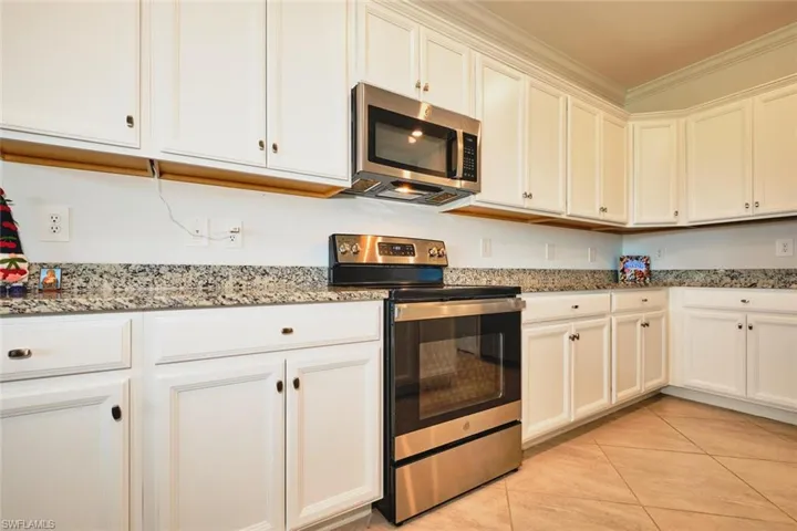 Kitchen with stainless steel appliances, white cabinetry, dark stone counters, light tile patterned floors, and crown molding