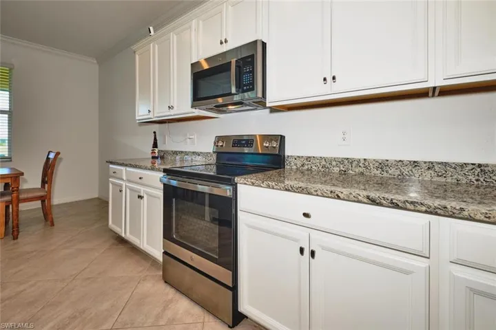 Kitchen with stainless steel appliances, white cabinetry, crown molding, dark stone countertops, and light tile patterned floors