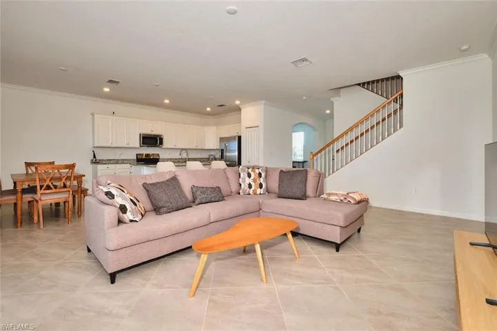 Living area with crown molding, recessed lighting, stairway, light tile patterned flooring, and arched walkways