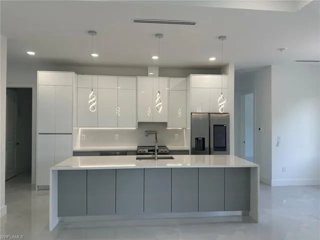 Kitchen with light tile patterned flooring, tasteful backsplash, white cabinets, a large island, and stainless steel refrigerator with ice dispenser
