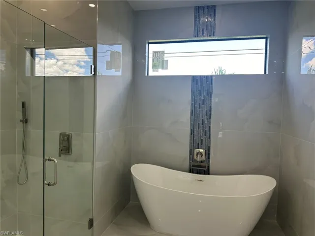 Bathroom featuring tile patterned floors, independent shower and bath, tile walls, and a wealth of natural light