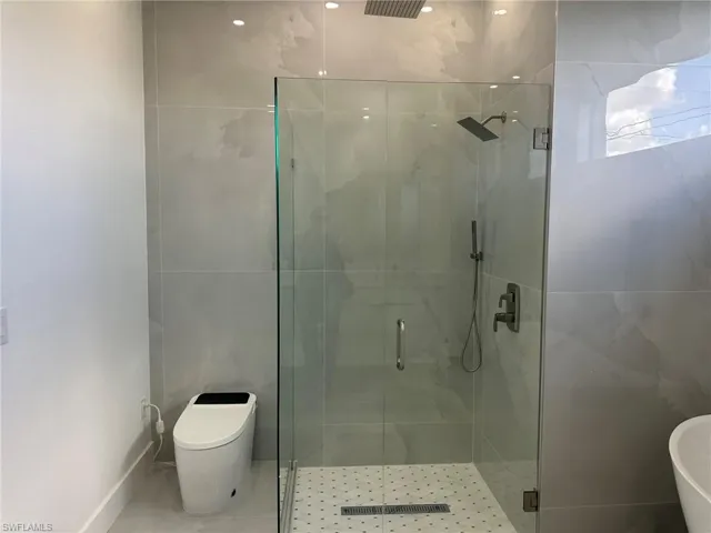 Bathroom featuring tile walls, tile patterned floors, a shower with door, and toilet