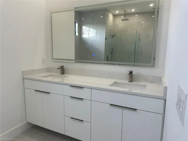 Bathroom featuring tile patterned flooring, dual vanity, and an enclosed shower