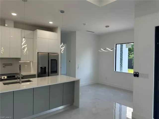 Kitchen with decorative light fixtures, white cabinets, light stone countertops, stainless steel fridge, and light tile patterned floors