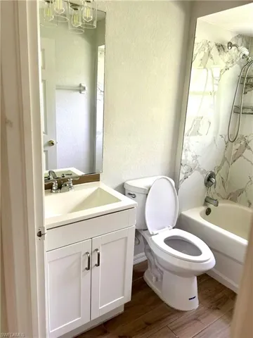 Bathroom featuring a textured wall, bathing tub / shower combination, vanity, and dark wood-type flooring
