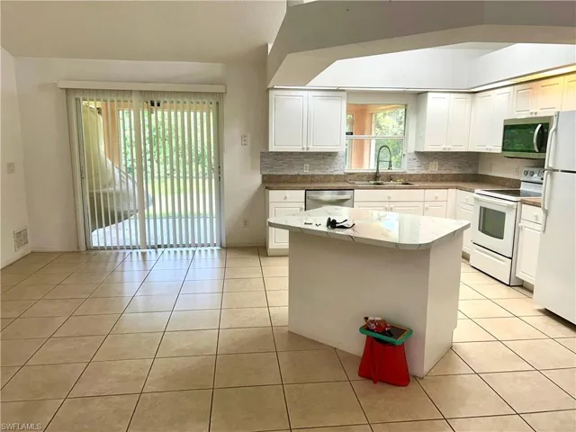 Kitchen with appliances with stainless steel finishes, light tile patterned floors, white cabinetry, backsplash, and a center island