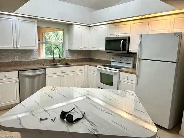 Kitchen featuring appliances with stainless steel finishes, white cabinets, decorative backsplash, light tile patterned floors, and a kitchen island