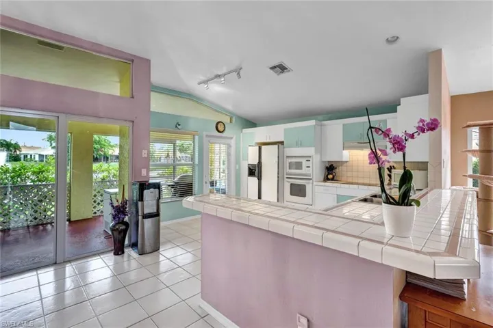 Kitchen with backsplash, rail lighting, tile counters, white appliances, and lofted ceiling