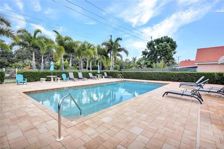 View of community pool with a patio area and tennis courts. This community is gated.
