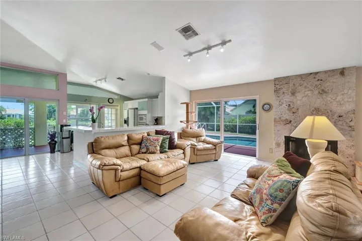 Tiled living room featuring vaulted ceiling and track lighting, nice side sliding glass doors for natural light and easy pool access