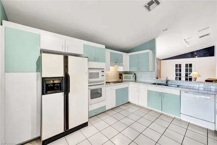 Kitchen featuring white appliances, blue cabinetry, backsplash, sink, and vaulted ceiling