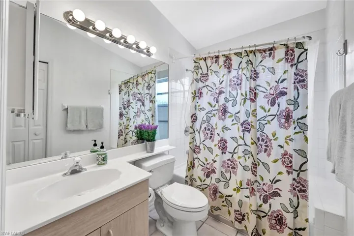 Full bathroom with oversized vanity, lofted ceiling, toilet, tile flooring, and shower / tub combo with curtain