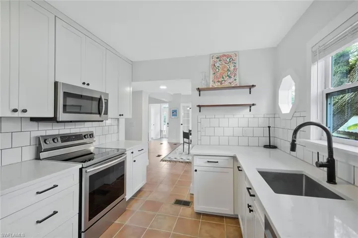 Kitchen with stainless steel appliances, open shelves, light stone countertops, and white cabinets