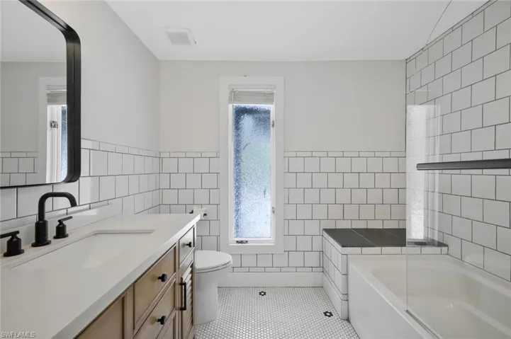 Full bath with vanity, a bath, tile walls, wainscoting, and light tile patterned floors