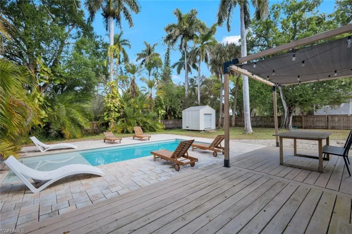 View of pool with a fenced backyard, a deck, a storage unit, and patio surround
