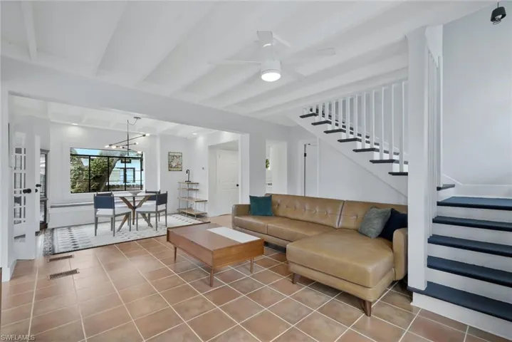 Tiled living area featuring a ceiling fan, beam ceiling, and a chandelier