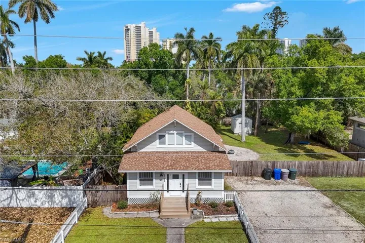 View of front of property with roof with shingles, covered porch, a fenced front yard, and view of wooded area