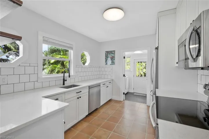Kitchen with stainless steel appliances, decorative backsplash, white cabinetry, light stone counters, and light tile patterned flooring