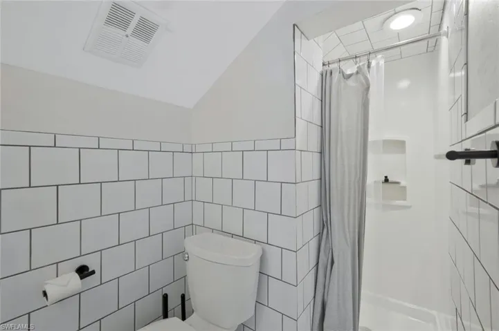 Bathroom featuring a stall shower, tile walls, and vaulted ceiling