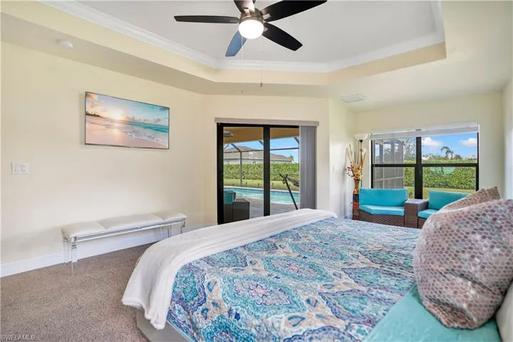 Carpeted bedroom featuring access to exterior, a tray ceiling, ceiling fan, and ornamental molding