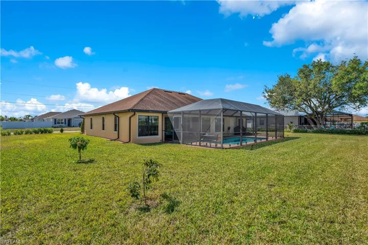 Back of property with an outdoor pool, a sunroom, glass enclosure, a lawn, and a patio area