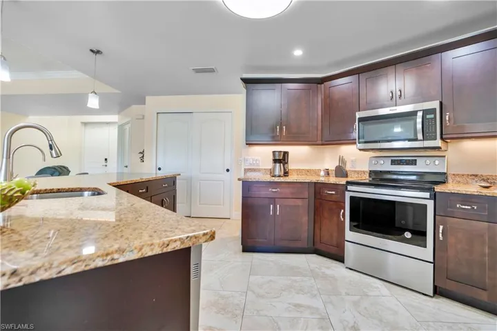 Kitchen with stainless steel appliances, dark wood finish cabinetry, decorative light fixtures, light stone countertops, and ornamental molding