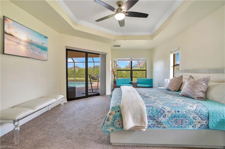 Carpeted bedroom with crown molding, access to exterior, a raised ceiling, multiple windows, and ceiling fan