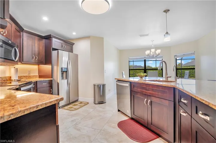 Kitchen with stainless steel appliances, dark wood finish cabinetry, light stone countertops, and suspended lighting