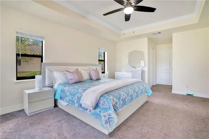 Bedroom featuring ornamental molding, carpet floors, ceiling fan, and a tray ceiling