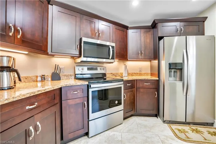Kitchen featuring stainless steel appliances, light stone counters, and dark wood finish cabinetry
