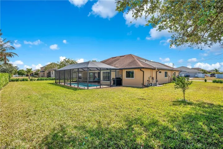 Rear view of house with a sunroom, a lawn, a lanai, an outdoor pool, and stucco siding