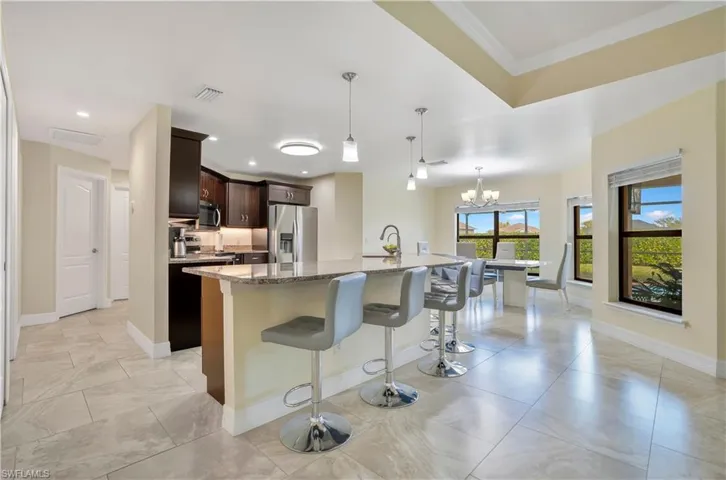 Kitchen featuring dark wood finish cabinetry, light stone countertops, a kitchen bar, stainless steel appliances, and a center island with sink