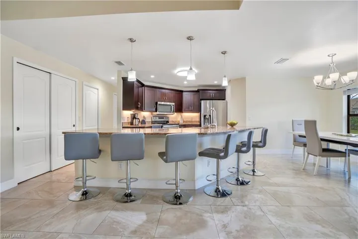 Kitchen with a breakfast bar area, light stone counters, stainless steel appliances, dark wood finish cabinetry, and hanging lights