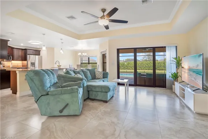 Living room featuring a tray ceiling, hanging lights, ceiling fan, and crown molding