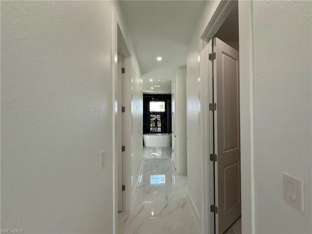 Corridor with baseboards, recessed lighting, marble finish floor, and a textured wall