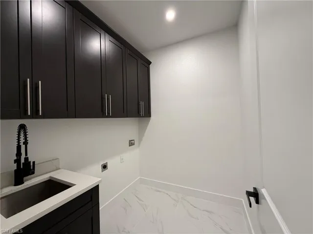 Washroom featuring hookup for an electric dryer, marble finish floor, a sink, baseboards, and cabinet space