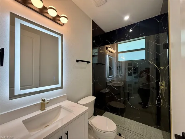 Full bathroom featuring vanity, a marble finish shower, and a textured wall