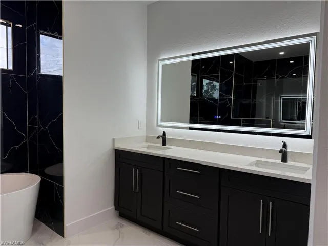 Bathroom with a freestanding bath, double vanity, marble finish floor, and a sink