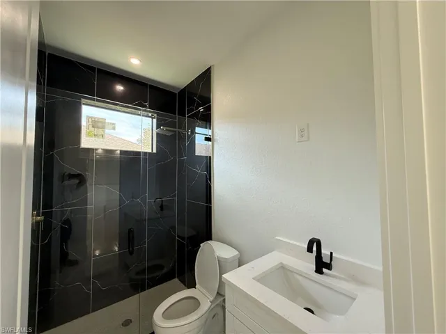 Bathroom featuring a marble finish shower, toilet, vanity, and a textured wall