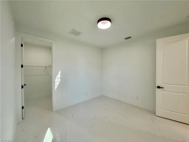 Unfurnished bedroom featuring a walk in closet and light marble finish flooring