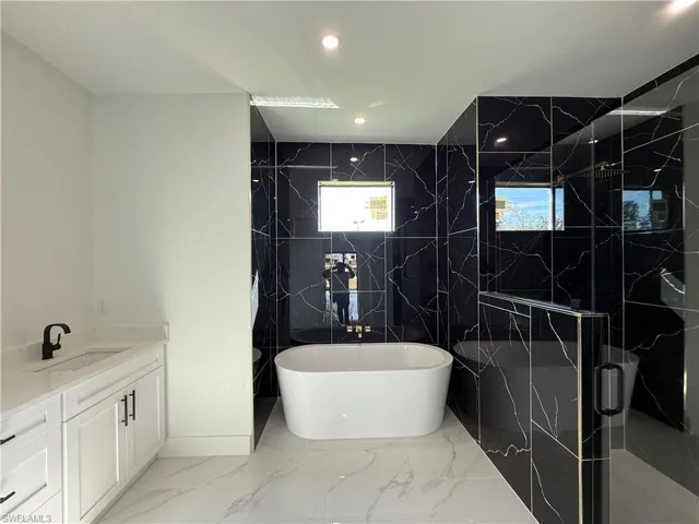 Full bath featuring a freestanding tub, vanity, a stall shower, recessed lighting, and marble finish floor