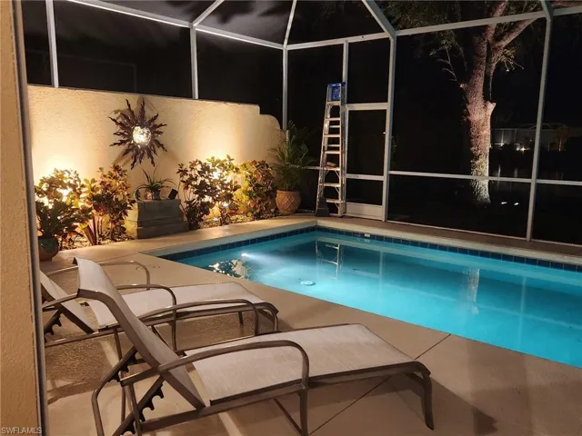 Pool at night featuring a lanai, an outdoor pool, and a patio