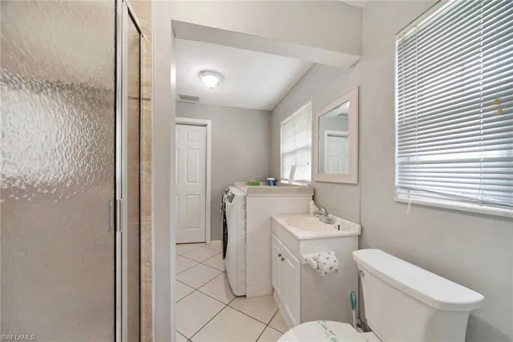 Bathroom for bedroom 2. attached is separate washer and dryer, tile patterned flooring, toilet, vanity, and a shower with glass door.