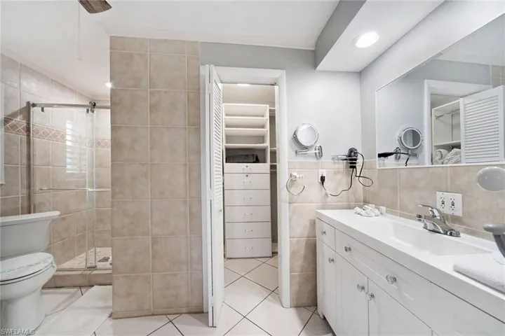 Primary suite Bathroom with an enclosed shower, tile patterned floors, and tile walls, large vanity and walk in closet.