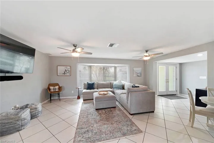 Tiled living room with bay windows and French entry doors and ceiling fans.