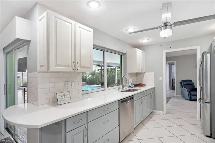 Kitchen with tasteful backsplash, stainless steel appliances, sink, white raised panel  cabinets, and gray lower cabinets. convenient pass through window to patio.