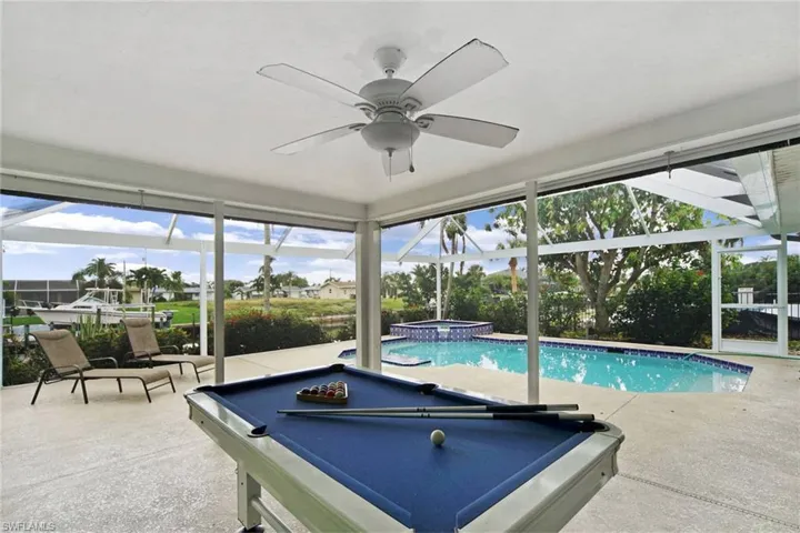 View of pool featuring large screen enclosure, and heated spa with waterfall, ceiling fan, and a pool table.